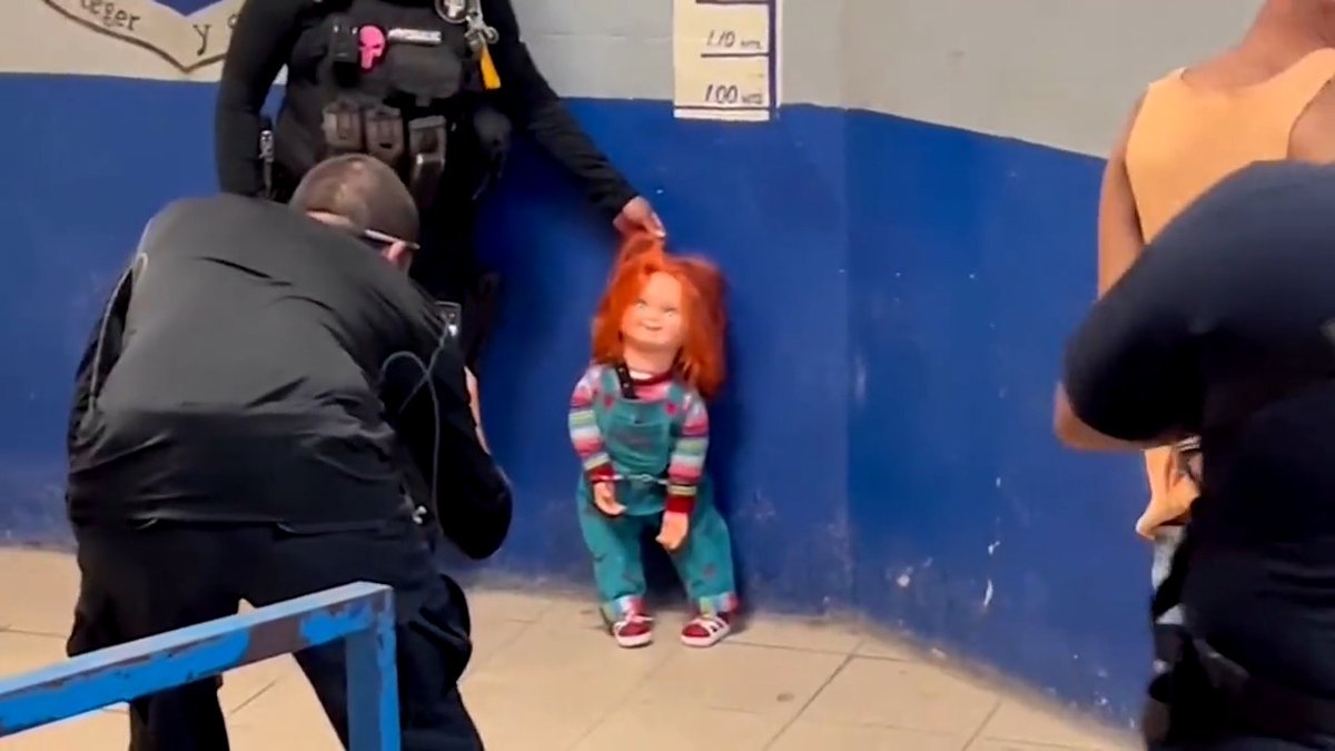Handcuffed, a knife still sticking out of his overalls, Chucky hunches against the wall as police hold him by his bright orange hair to take his mug shot. The 'demon doll' and its owner were arrested in Mexico for scaring people and demanding money