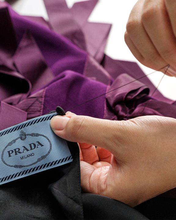 The Prada Fall/Winter 2024 sablé dress is meticulously covered in hand-knotted and manually-embroidered satin bows, a masterwork of craftsmanship characterized by techniques that create movement and shape. The process (cont)