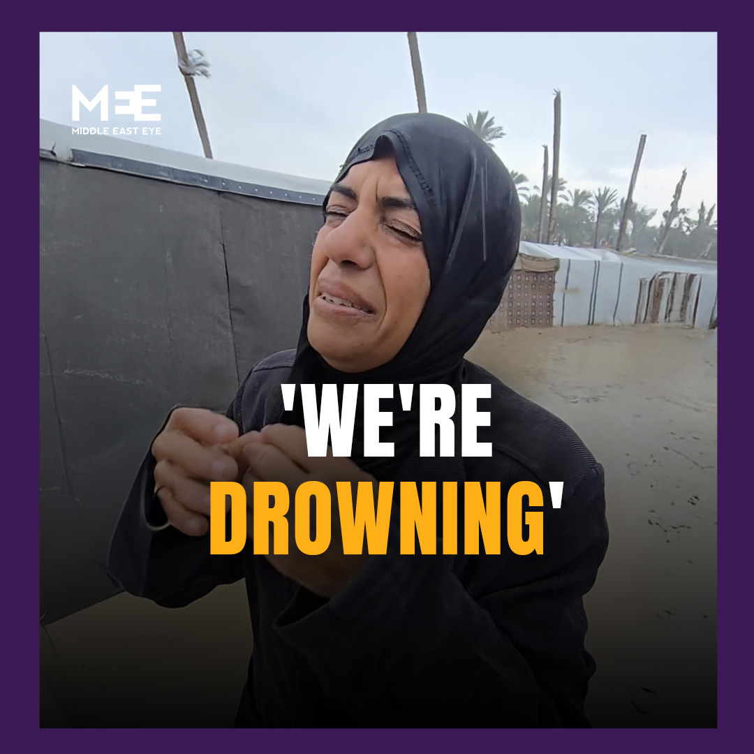 A Palestinian woman stood in a flooded displacement camp in Gaza, explaining how she was forced to stand all night during the heavy rainfall as her tent became submerged, with her family’s mattresses floating in the water.