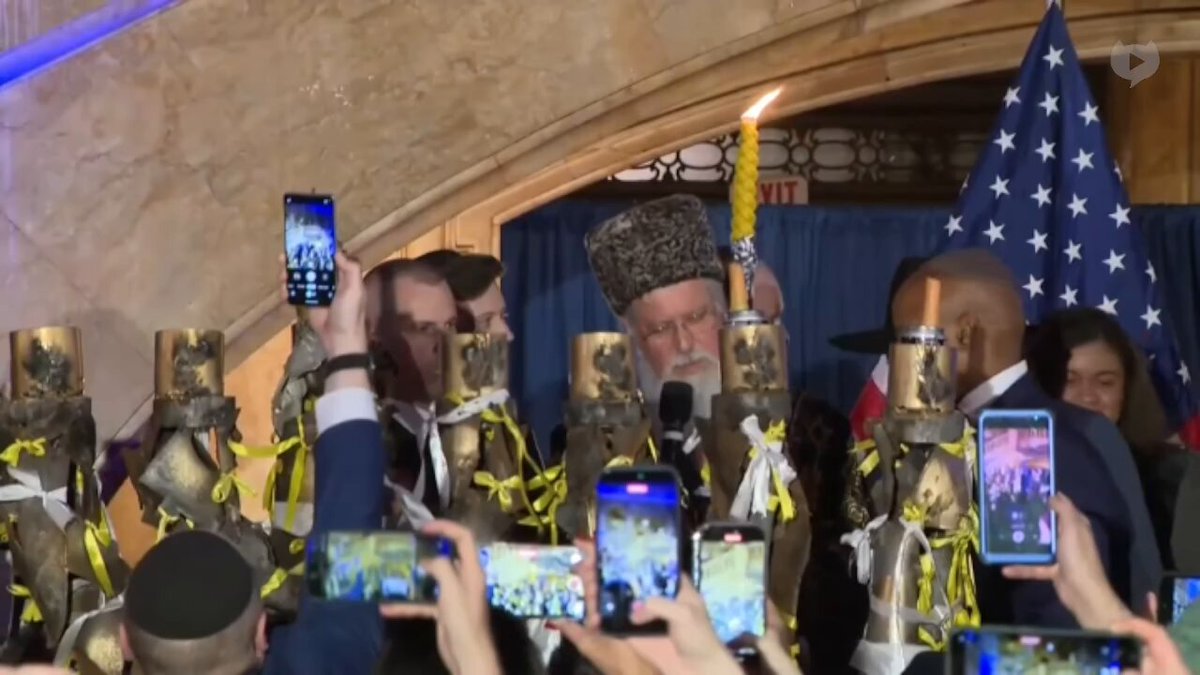NOW - New York City mayor Eric Adams lights a giant menorah with a Rabbi while wearing a kippah.