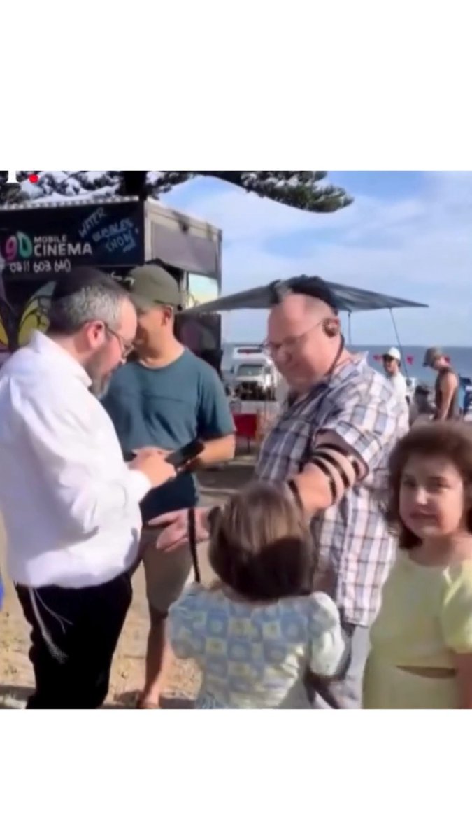 In this video, 10-year-old Matilda watches Rabbi Eli Schlanger wrap tefillin around her father Michael’s arm at the Bondi Beach Chanukah party. It’s a sacred ritual, thousands of years old, meant to connect heart and mind to G-d. Matilda stands close in her yellow dress, witnessing an ancient act of love, tradition, and faith. Soon after, Matilda, Rabbi Schlanger, and 13 others were murdered in cold blood at Bondi Beach. Jews were killed just for being Jewish; for celebrating a Jewish holiday. We mourn with the families and loved ones of the victims of the Bondi Beach massacre.