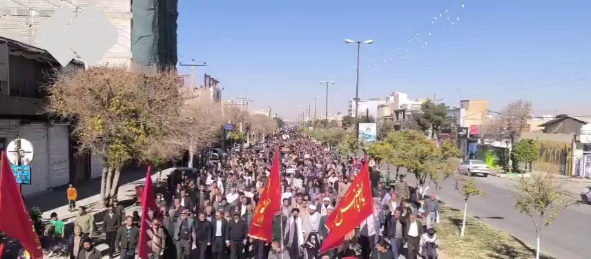 A pro-regime march in Tehran: mostly male crowd waving Iranian flags and chanting loyalty slogans, staged as a show of support for the government.