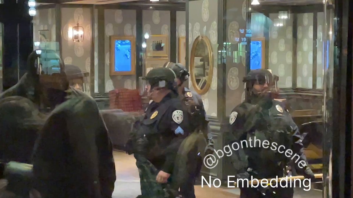 Police with batons and face shields inside Graduate by Hilton Minneapolis, as anti-ICE protesters demonstrate outside the hotel