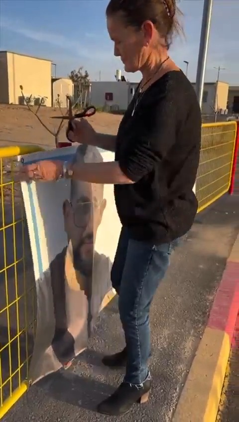 In Kibbutz Be'eri, a community that was horrifically devastated by Hamas on October 7, 2023, residents Nira Sharabi and Raaya Rotem remove a poster of Ran Gvili. Nira's husband Yossi Sharabi z”l was murdered in Hamas captivity and returned to Israel in October 2025, and Raaya is a survivor of Hamas captivity.