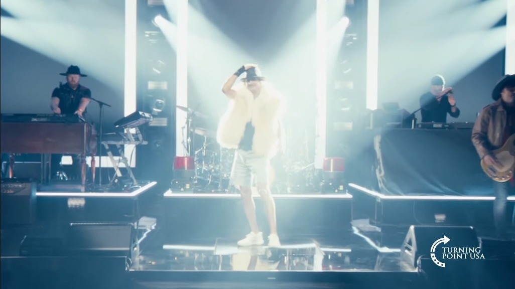 Kid Rock screeches while wearing a fur vest, jorts, and a fedora at the Turning Point USA halftime show.