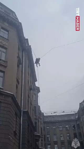 Rusya'da binanın çatısında kar temizliği yapan bir kişi, yere düşmekten elektrik tellerine takılarak kurtuldu.