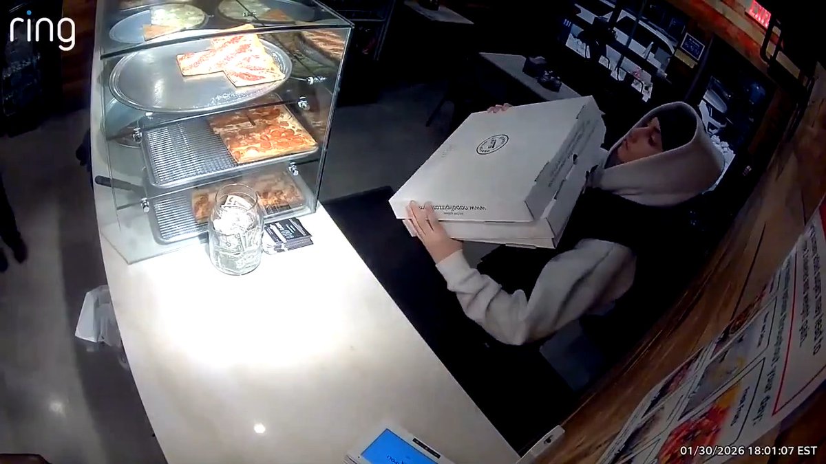 A pizza shop guy teaches a kid how to carry pizza boxes so the pies don’t get ruined.