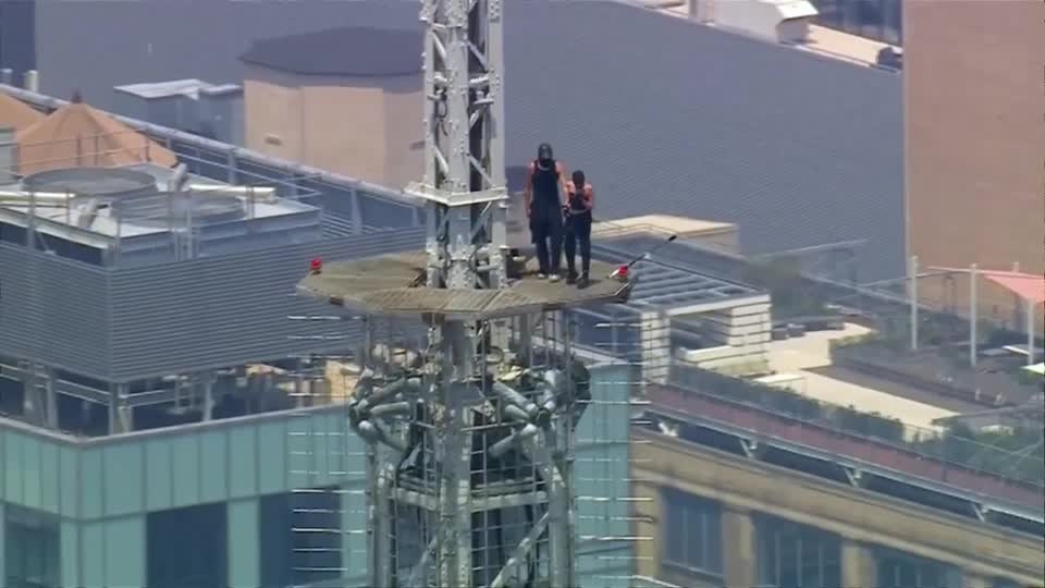 2人は黒いノースリーブ姿で、地上約443メートルの高さにあるビルのアンテナ付近にしがみついた。