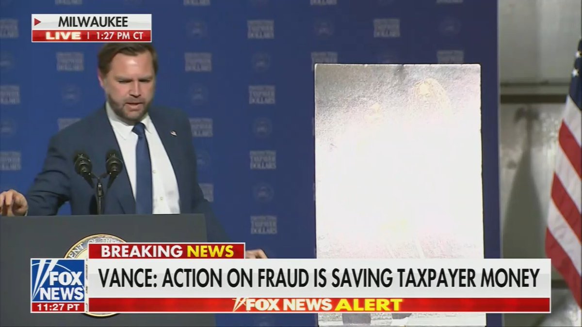 JD Vance flips around a poster to show his audience but the glare is so bad it is impossible to see what's being depicted