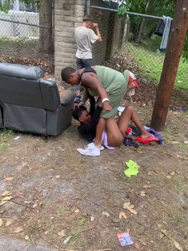 Two black women fights dirty on the street, while bystanders watch in amusement.