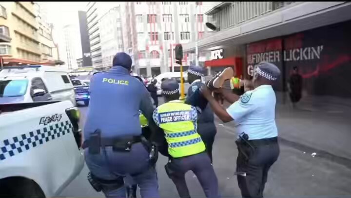 Five police officers are carrying one man; I believe he is Nigerian. 🇬