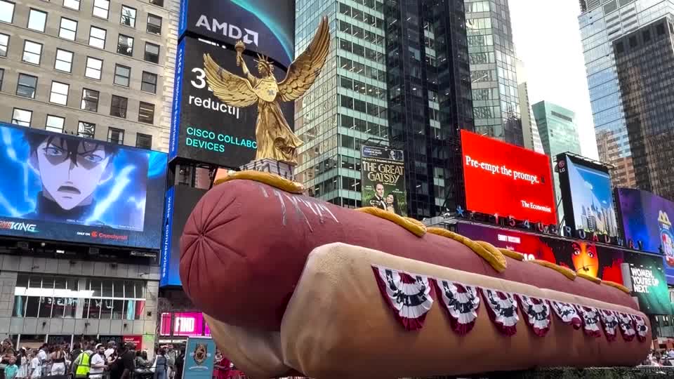 A 65-foot-long hot dog sculpture returned to Times Square for the US's 250th anniversary, featuring flag bunting, camouflage netting, and a gold Lady Liberty figure held together by duct tape