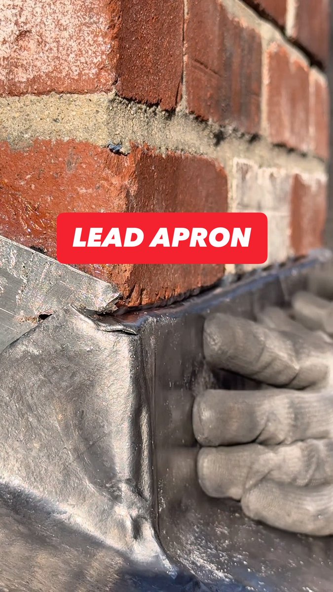 Lead apron going in around a brick chimney. The soft metal is shaped and fitted to create a watertight transition between roof and brick.