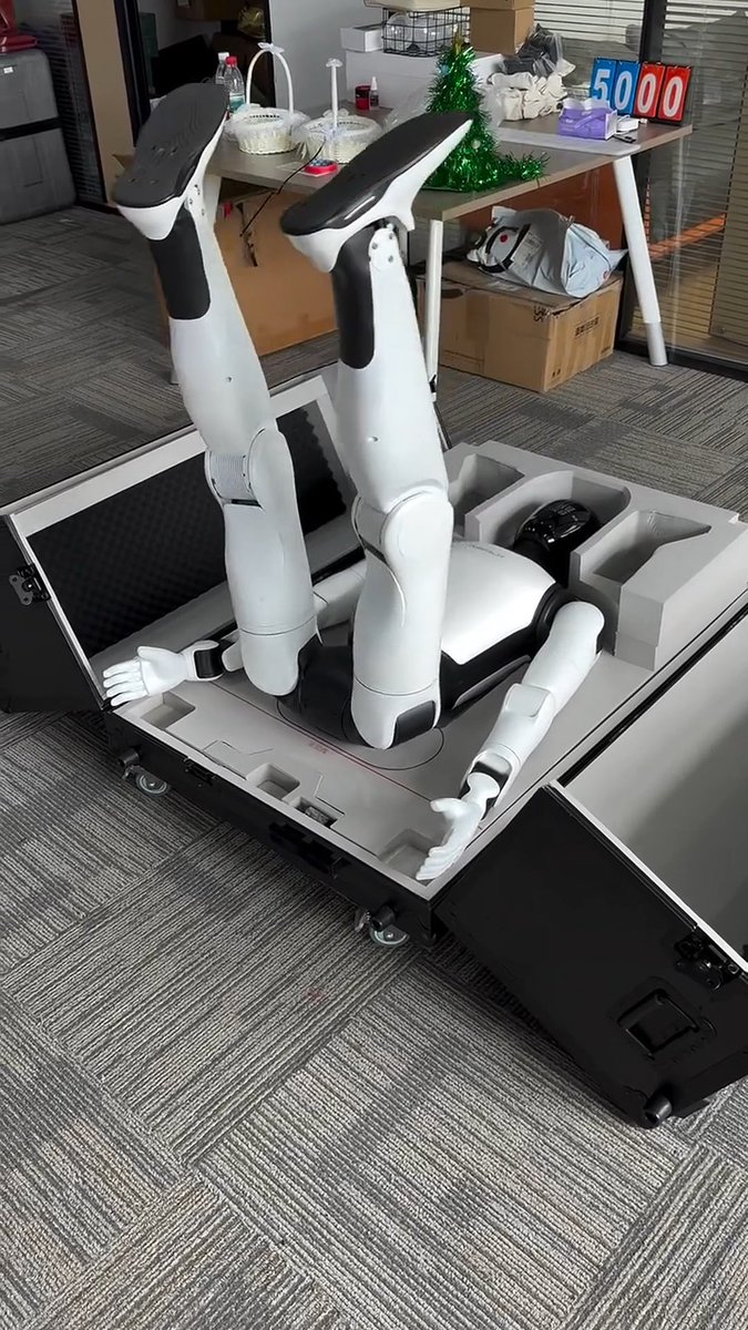 ⚠️ THIS ROBOT WOKE ITSELF UP IN A CARDBOARD BOX. NOBODY TOLD IT TO. A robot just unboxed itself. No hands. No engineers. No stage. No keynote. It woke up lying flat on its back inside a foam-lined shipping case in the middle of an ordinary office — desks, a small Christmas tree, nothing staged. Its legs bent upward, then extended, pushing it out of the case. It rolled, braced with its arms, lifted its torso, and stood up to full height right next to the open box it arrived in. Chinese subtitles ran the entire time as the robot calmly narrated its own startup: warning that it was about to move, asking not to be touched, confirming its position, then requesting that the packaging be cleared so it could start work. This is AGIBOT. The company that shipped more than 5,168 humanoid robots in 2025 — more than any competitor globally — and hit its 15,000th unit produced by mid-2026. Not a staged reveal. Not a product launch. Just a robot that ships itself in a box and gets up on its own. The unboxing used to be the boring part. Now it’s the demo.