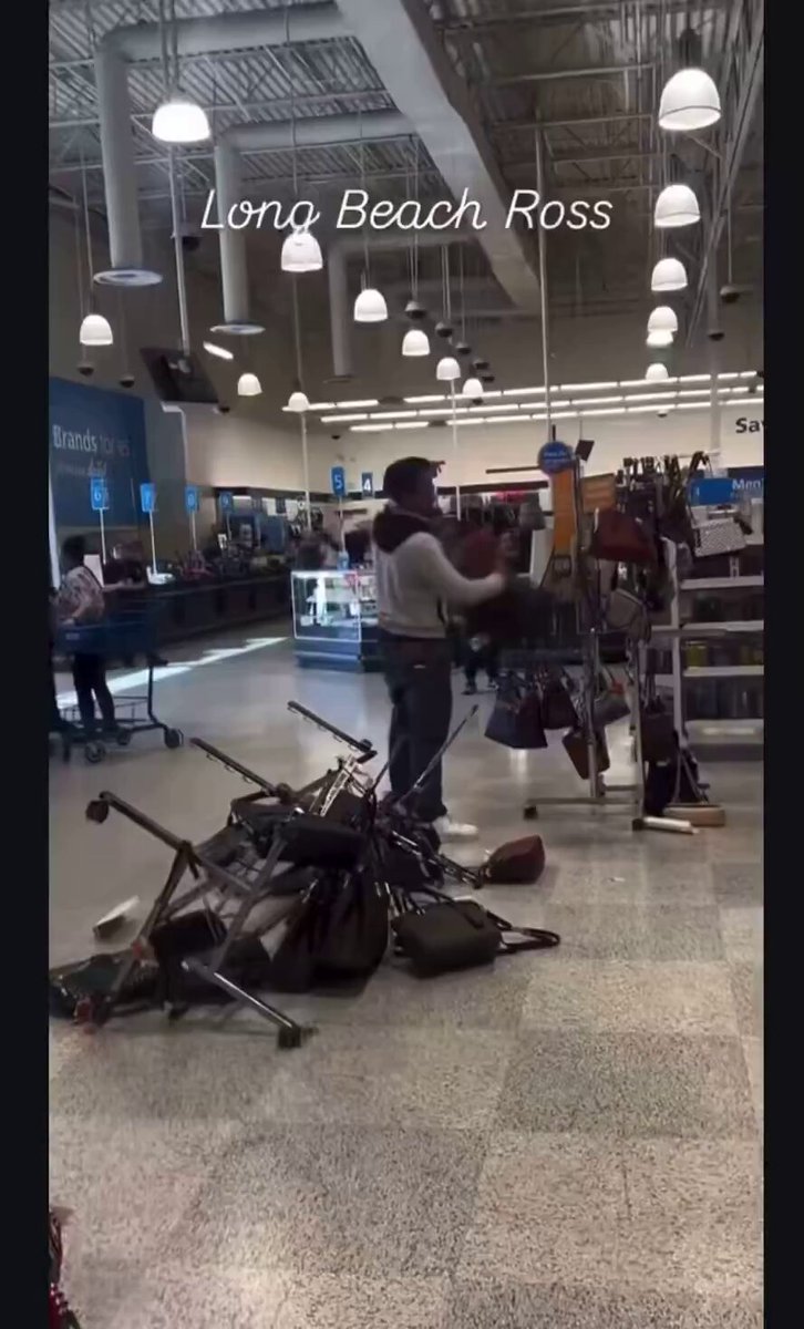 Two guys casually shoplifting purses despite alarm in the background