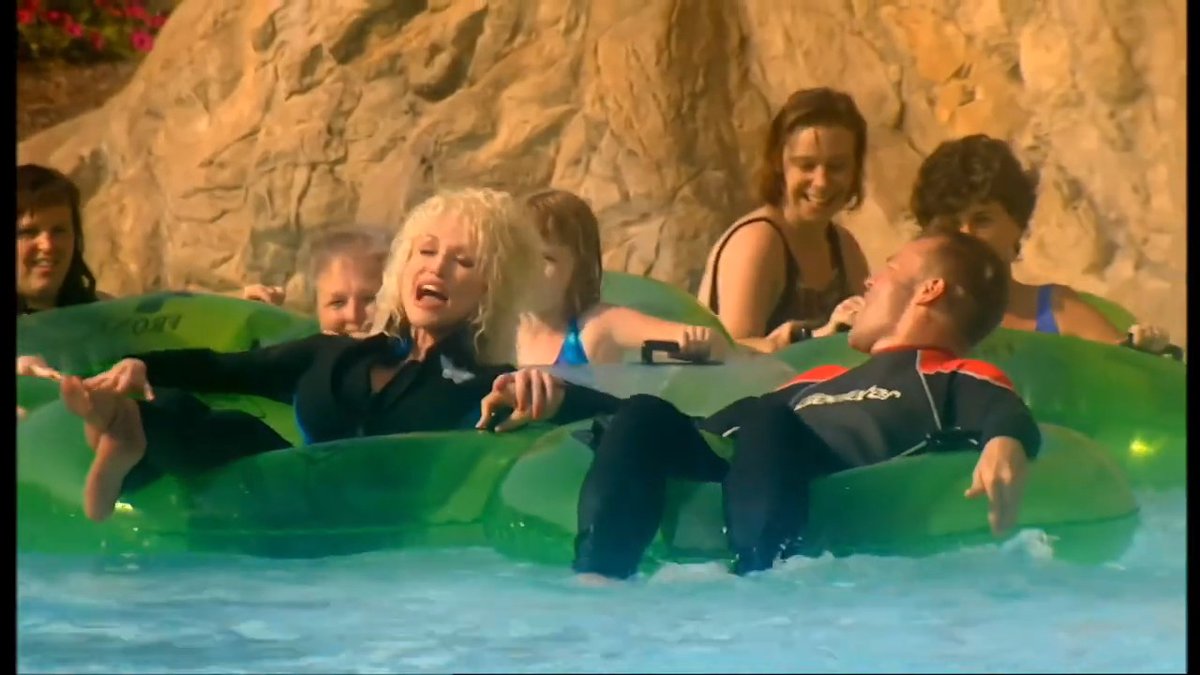 DOLLY PARTON ISLANDS IN THE STREAM Dolly Parton turning a water ride into a full-blown music video is something I genuinely did not expect. This starts off looking like a normal day at Dollywood, and then suddenly Dolly is floating through the water while Islands in the Stream is playing like this was the most expensive music video ever made. And the funniest part is how seriously the whole thing is treated. She's surrounded by people on tubes, water flying everywhere, and somehow Dolly still looks completely at home in the middle of it. Then Graham gets involved and the whole situation becomes even more ridiculous. It has that unmistakable early-2000s television energy where someone basically says, We have Dolly Parton at Dollywood… let's just put her in the water and see what happens. And honestly? It works. Dolly could probably walk into a supermarket, start singing, and somehow make the entire building feel like a stage.