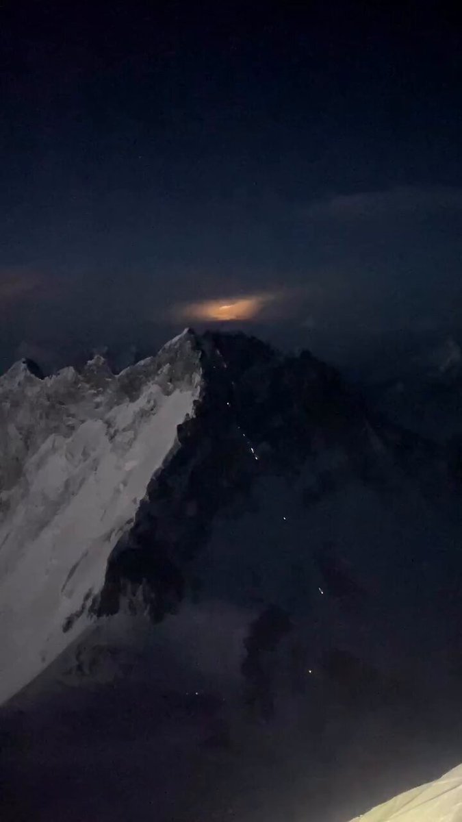 A long line of Trekkers ascend the ‘Death Zone’ on Mt Everest as lighting roars in the distance.