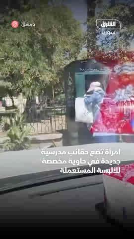 امرأة تضع حقائب مدرسية جديدة في حاوية مخصصة للألبسة المستعملة بأحد شوارع دمشق