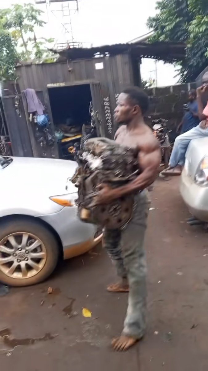 Nigerian mechanic shows off his strength as he single-handedly lifts a car engine and walks with it.