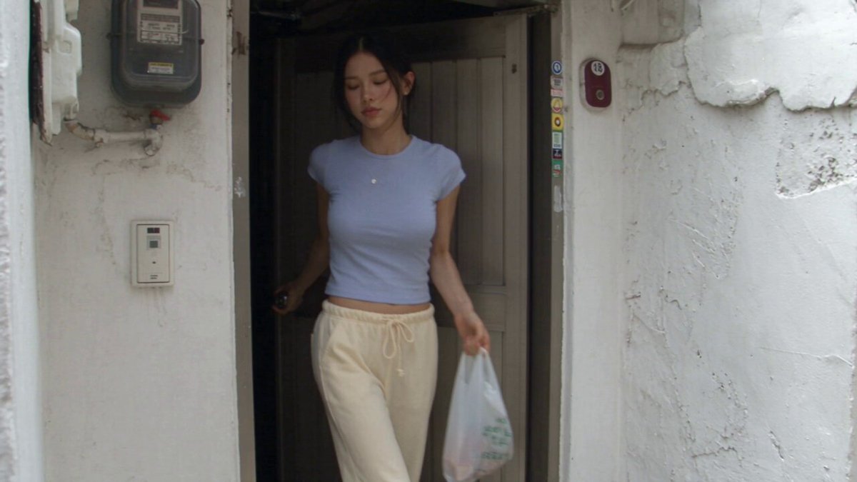 Baddie is back. Obviously on Sunday Seedance 2.5 Prompt : Create a 30-second, 1080p ultra-realistic personal home-video showing an ordinary summer Sunday afternoon in the life of a young Korean woman. No reference image. Young Korean woman, early 20s, naturally pretty, realistic skin texture, minimal makeup, long black hair in a messy side ponytail, fitted pastel-blue short top, loose cream pajama-style pants, black sneakers and simple silver necklace; maintain identical appearance throughout. Set in a quiet older Seoul residential neighborhood with narrow concrete lanes, small homes, old walls, potted plants, bicycles, utility poles, overhead wires and children playing nearby. Raw early-2000s consumer DV camcorder aesthetic: strong handheld shake, imperfect framing, autofocus hunting, exposure shifts, faded colors, soft digital detail, mild noise, motion blur and accidental zooms; no polished cinematography. — LEAVING HOME: She steps outside carrying a small reusable shopping bag, locks the door, adjusts her ponytail and walks casually down the lane as a warm summer breeze moves her hair. — BISCUIT STOP: She notices a tiny neighborhood shop, buys a simple packet of biscuits, pays casually, then walks to a nearby bench and sits down. She opens the packet, eats a biscuit while watching the street, smiles at something happening nearby, then folds the empty packet and throws it neatly into a public dustbin beside the bench. — THE KITE: She notices several children struggling to retrieve a colorful kite stuck high in a tree; they try jumping and reaching for it but cannot get it down. She walks over, looks up, finds a safe low branch, carefully reaches the kite down and hands it to the children; they excitedly thank her. She smiles, takes the kite string for a moment and tries flying it herself; the kite rises awkwardly, dips in the wind, and she laughs while trying to control it. She finally gives the string back to the children, watches them happily run and fly the kite, waves goodbye and continues walking. — FINAL MOMENT: She turns into her own residential lane, walks toward home with the shopping bag, looks back at the children playing in the distance, smiles at the camera and says, “Happy Sunday.” She continues toward her house as the camera follows behind her, then the recording abruptly cuts to black; AUDIO: only children laughing, kite fluttering, footsteps, birds, summer insects, distant scooters, bicycle bells, neighborhood conversations, shop ambience and subtle camera-handling noise; no music or narration. NEGATIVE: No subtitles, captions, logos, watermarks, recognizable brands, identity changes, outfit changes, duplicated people, distorted hands, extra fingers, unrealistic kite physics, teleportation, object duplication, CGI look, artificial expressions, dramatic cinematic shots or polished commercial cinematography.