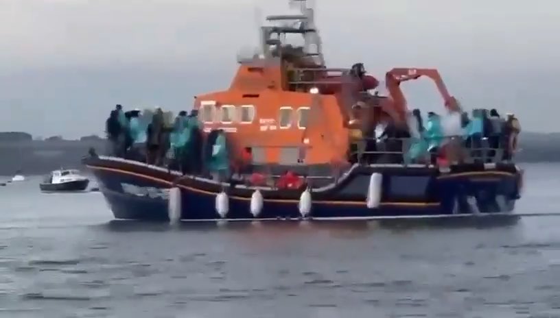 🚨NEW FOOTAGE: They used a blue light boat to stop the cameras Two men on a small boat off Eastney. RNLI on the beach with the arrivals. Official boat moves in to push them back so they can’t film it. You pay for the landing. You pay for the coaches. You pay for the boat that hides it.