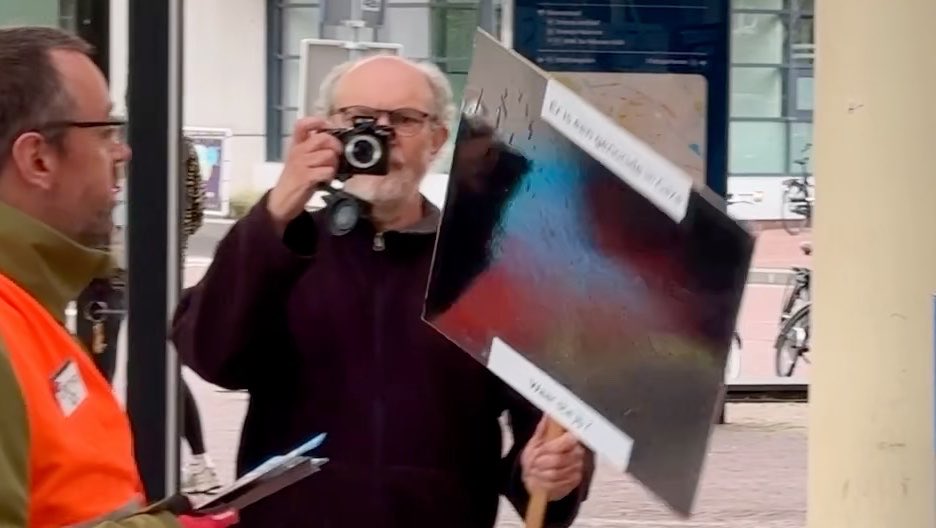 Kijk eens wie we daar hebben! De demonstrant die eerder nog agressief met een keukengerei-arsenaal op me afstormde, is creatief geweest op de knutselmiddag. Deze keer heeft hij met aluminiumfolie letterlijk én figuurlijk een bord voor z'n kop geknutseld om zich achter te verschuilen, terwijl hij stiekem met z'n cameraatje blijft loeren. Het verzet op Station Assen wordt steeds inventiever.